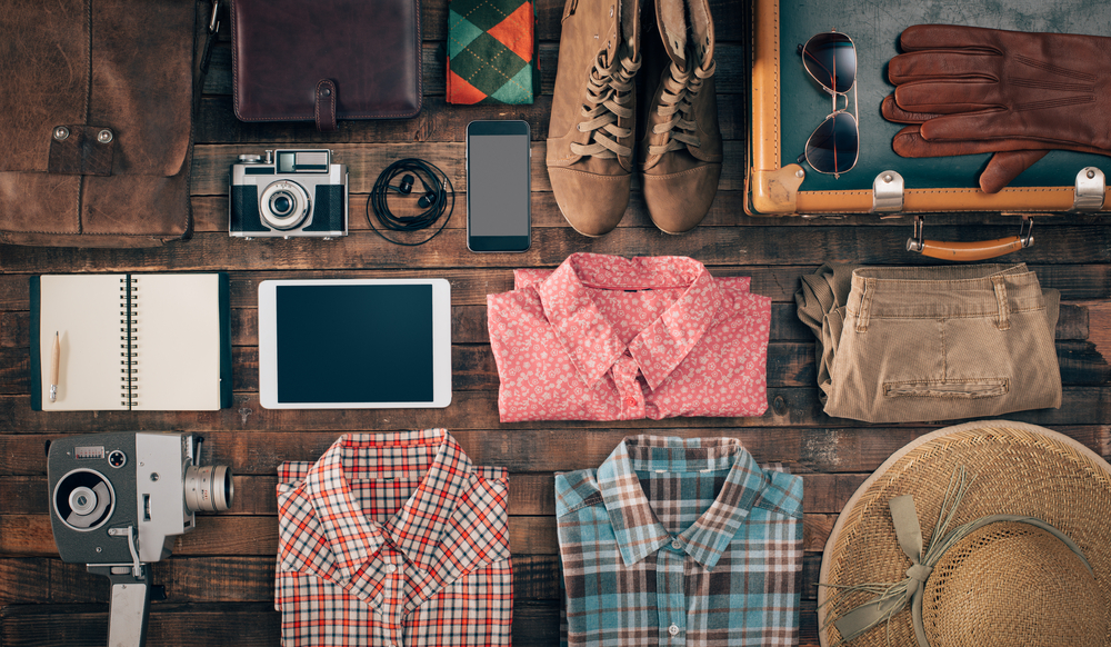 Assorted clothes and items laid out neatly on a wooden table next to a suitcase.