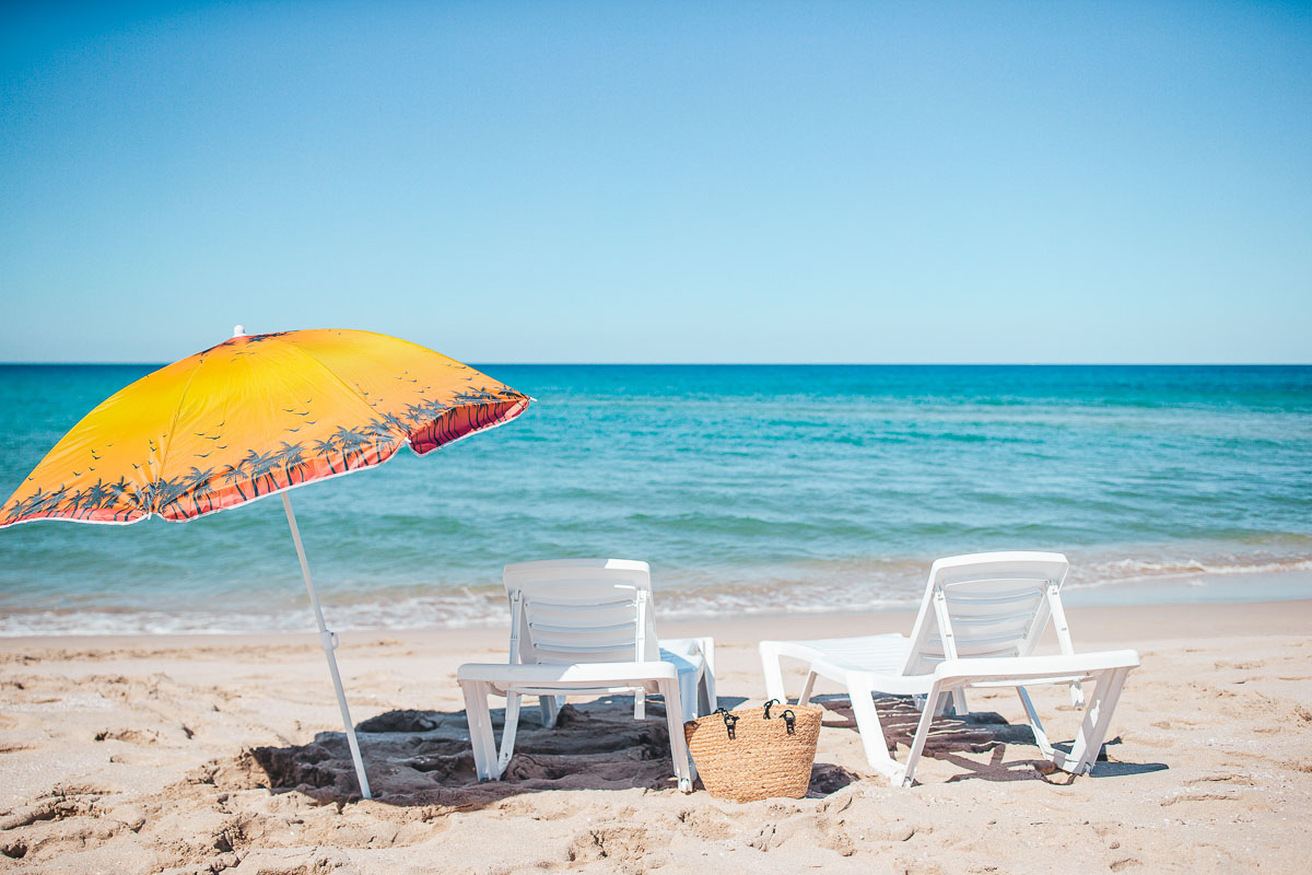 Beach sun beds and umbrella on white beach.