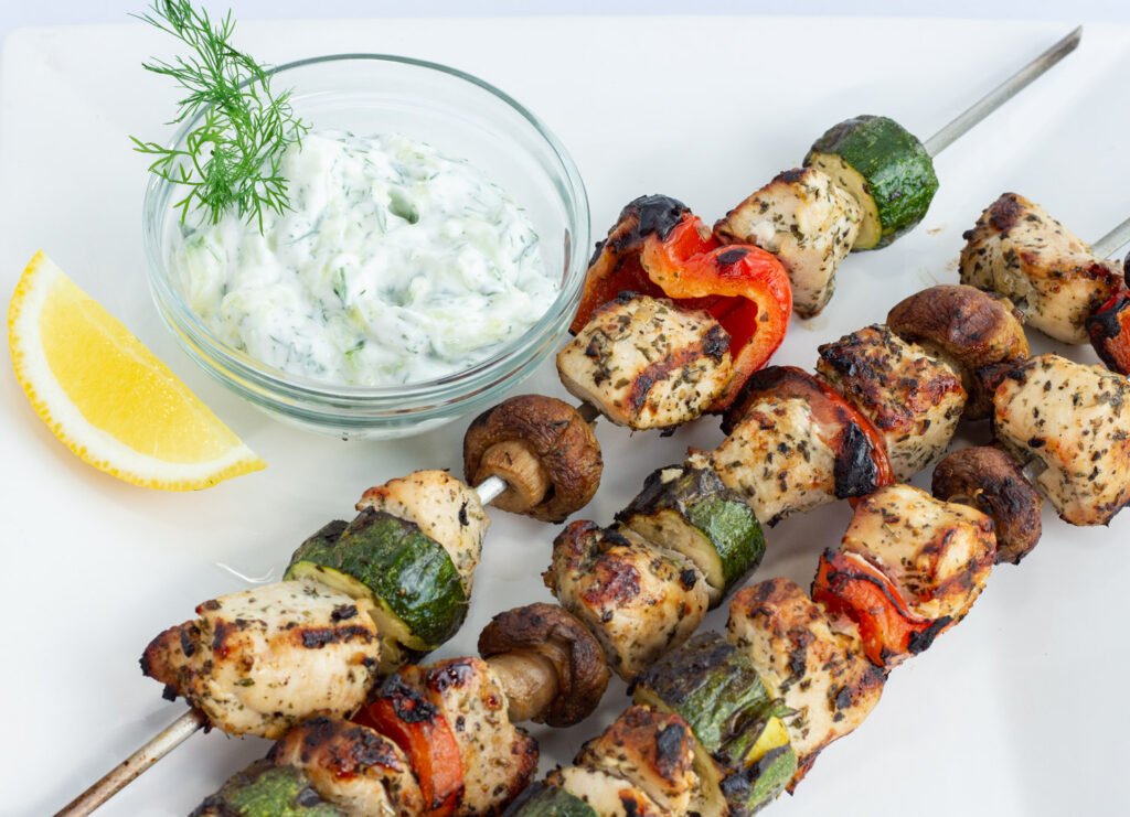 Chicken and Vegetable kabobs on a skewers with sauce nearby.