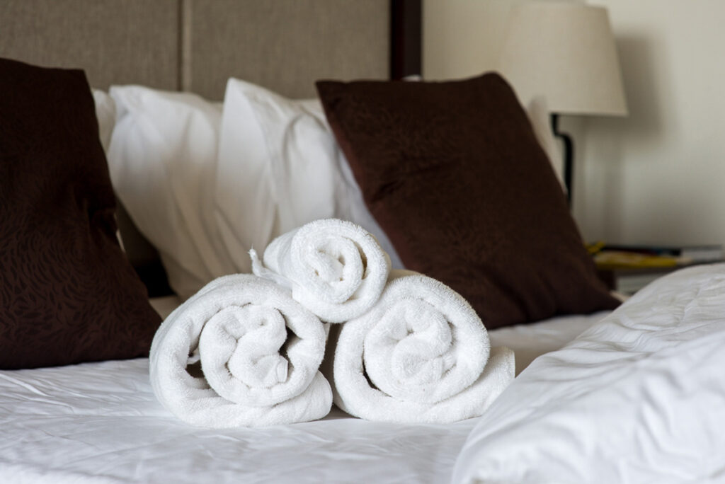 An image of rolled towels on a hotel room bed.