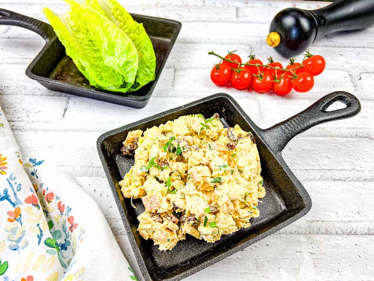 A pan of coronation chicken salad next to a plate of lettuce and tomatoes.