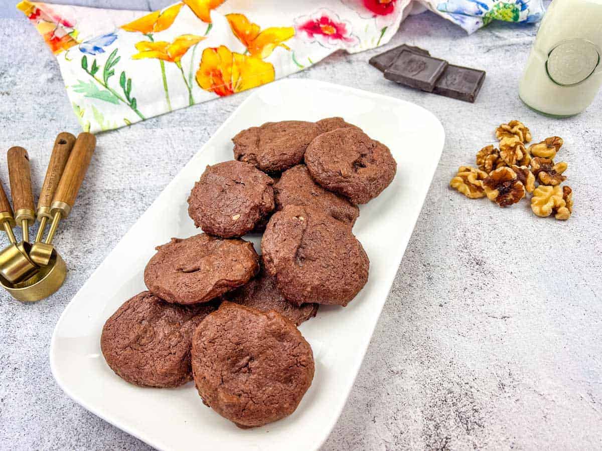 A plate of chocolate cookies with walnuts and chocolate pieces on the side.