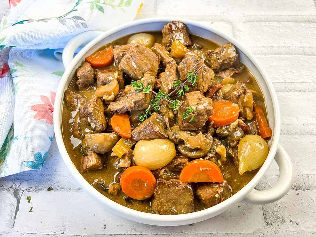 Beef bourguignon in a white bowl with thyme.