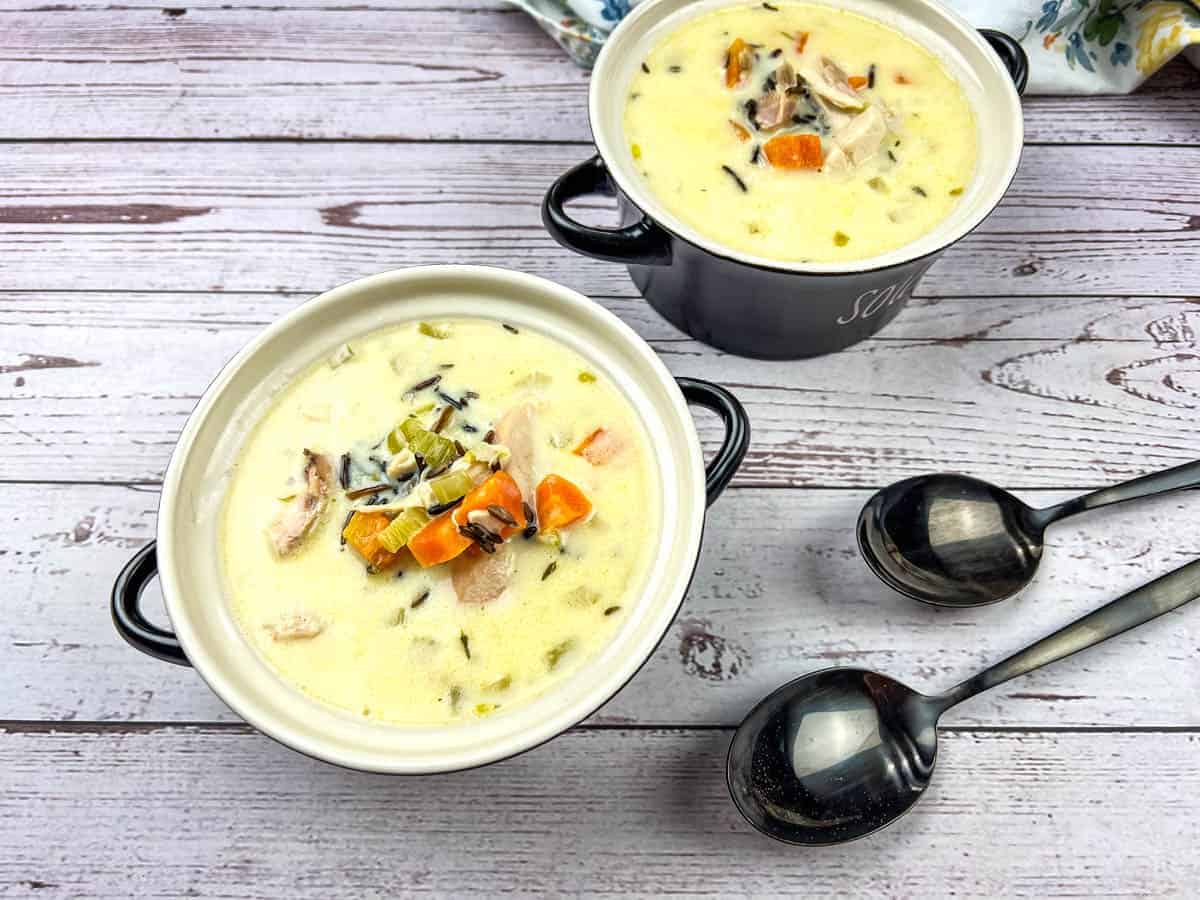 Two bowls of creamy chicken & wild rice soup on a wooden table.