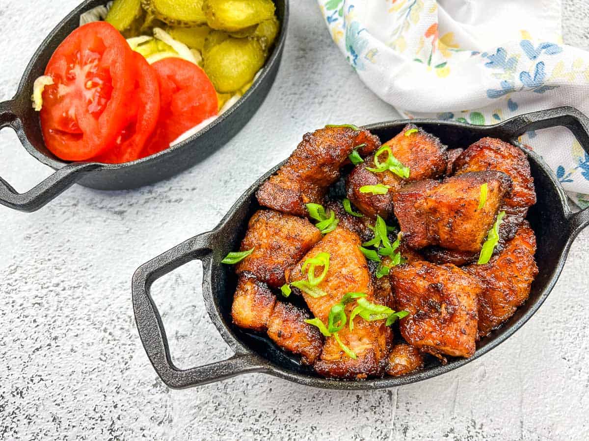 A plate of smoked pork belly burnt ends with tomatoes and pickles.