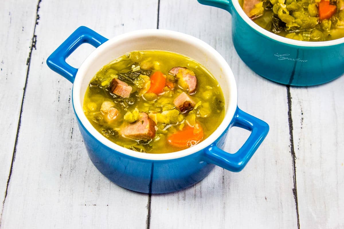 Two bowls of soup with ham, sausage, split peas and vegetables in them.