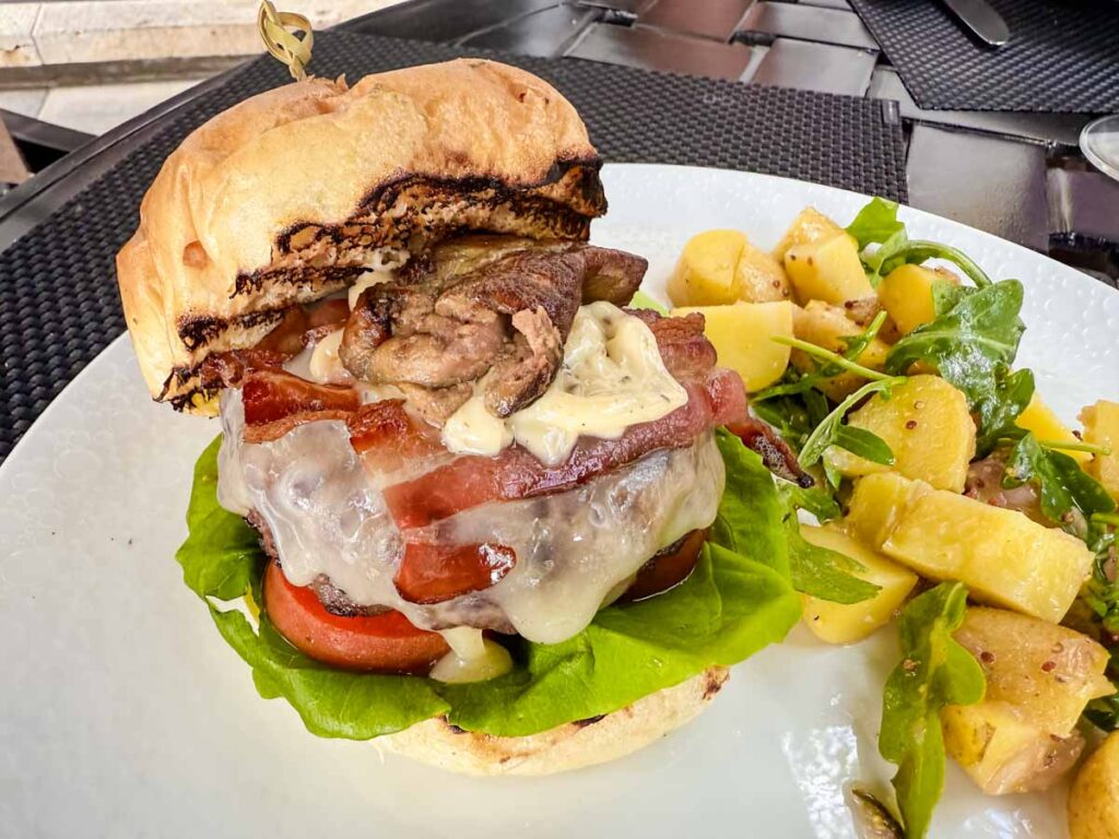 A burger with a thick bun, bacon, cheese, and veggies on the side.