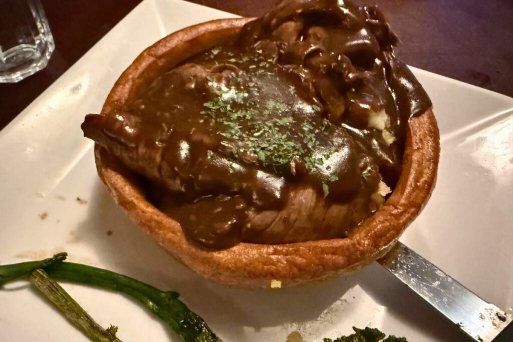 Roast beef inside a fluffy Yorkshire pudding on a plate.