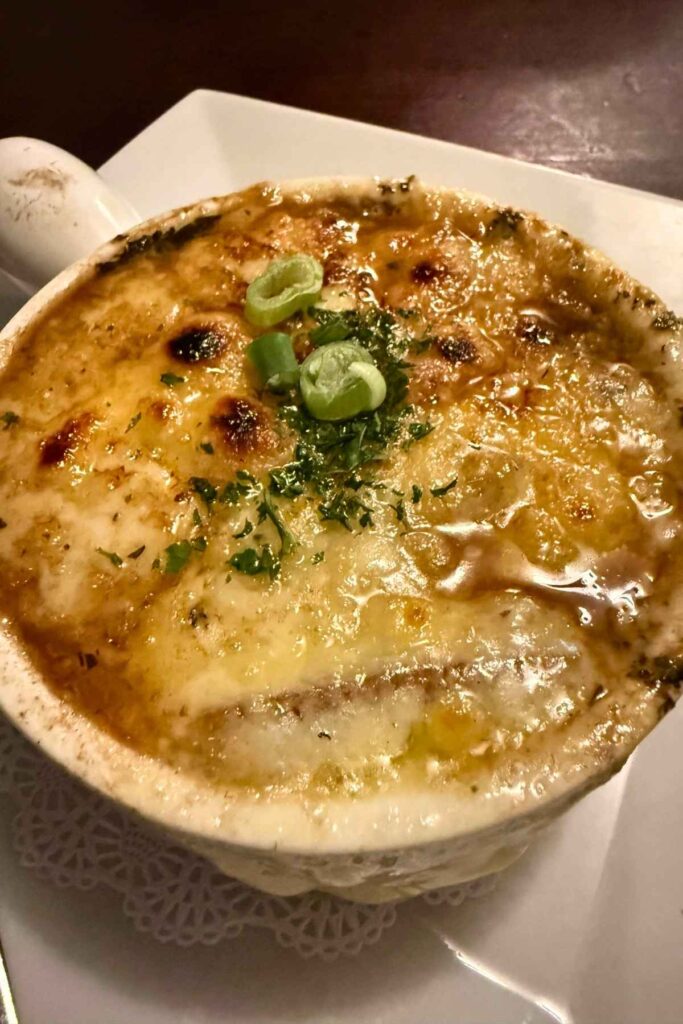Bowl of French Onion Soup garnished on top with herbs and melted cheese.