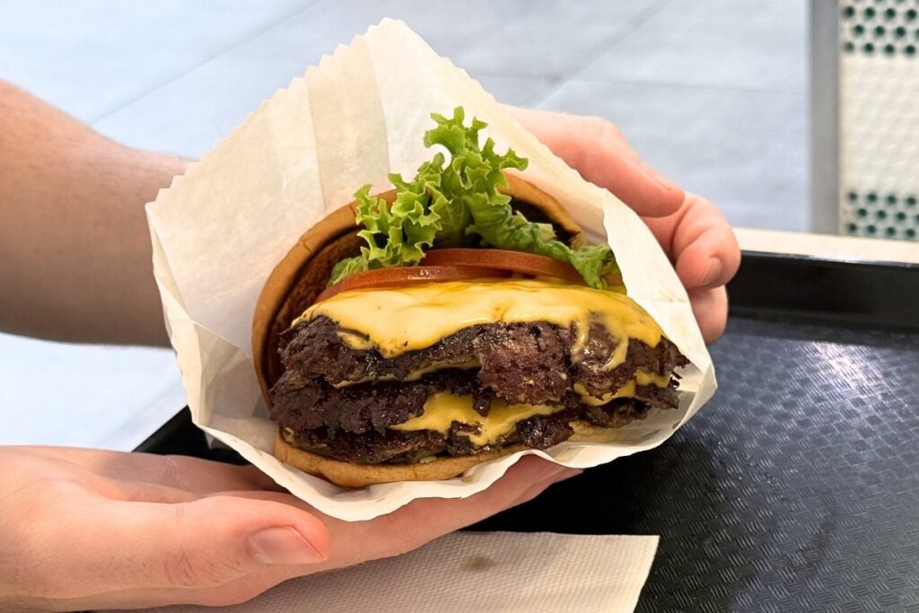A hand holding a cheesy burger filled with loaded patties.